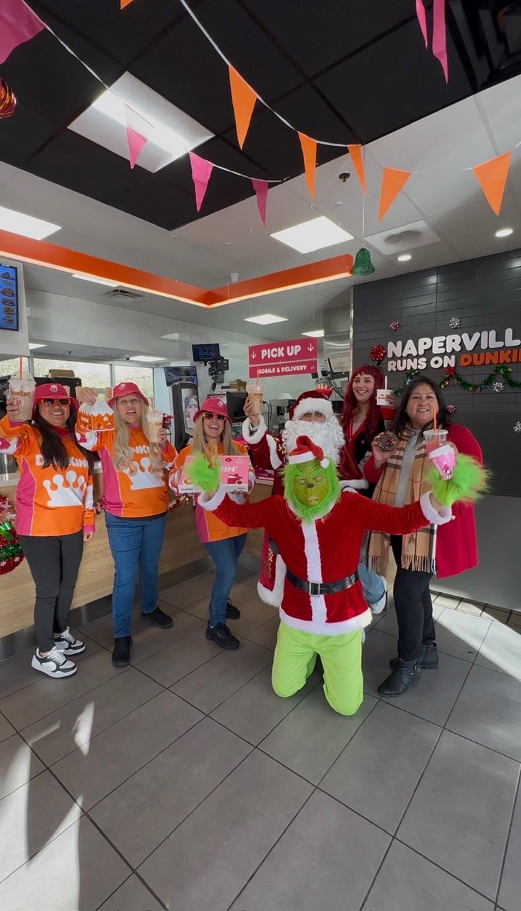 The PPP Donuts Network crew celebrating the holidays together in front of the 'Naperville Runs on Dunkin' wall