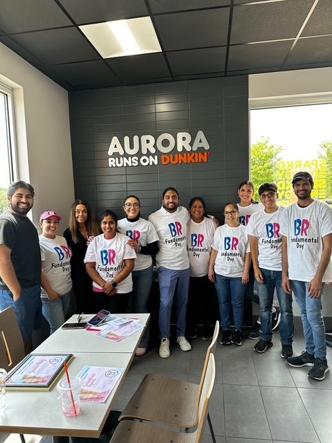The PPP Donuts Network crew together in front of the 'Aurora Runs on Dunkin' wall